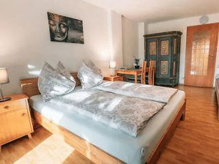 Spacious bedroom with a serene Buddha painting, minimalist decor, large windows, and a touch of traditional wooden furniture